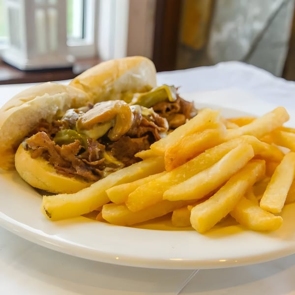 A cheesesteak sandwich with mushrooms and peppers, served with a side of golden french fries.