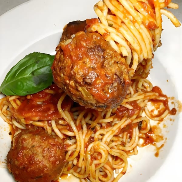 Spaghetti and meatballs with tomato sauce and a basil leaf on a white plate.