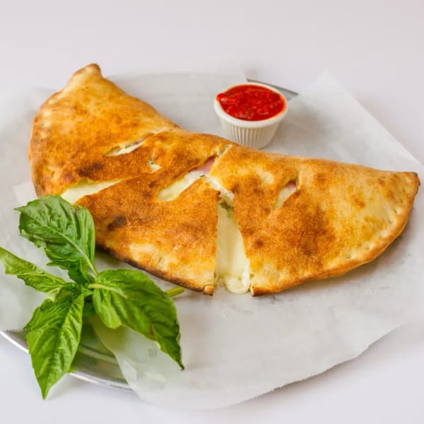 Golden-brown calzone, cut open with melted cheese oozing out, served with a side of marinara and fresh basil.