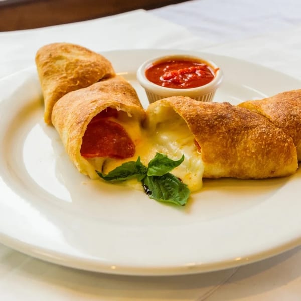 Golden-brown stromboli, cut open to reveal melted cheese and pepperoni, with a side of marinara sauce.